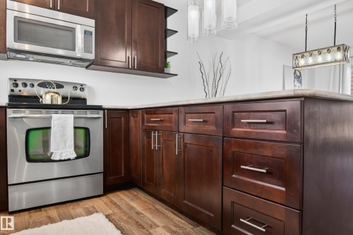 Kitchen featuring wood-finish flooring, stainless steel appliances, dark wood cabinetry with brushed nickel hardware, and light-toned countertops - 14522 56 Street, Edmonton, AB - Indoor Photo Showing Kitchen