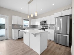 Modern kitchen featuring an island with a light countertop, white cabinetry, stainless steel appliances, grey subway tile backsplash, and wood-finish flooring - 