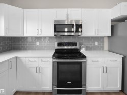 Kitchen featuring white shaker-style cabinetry, stainless steel appliances, a subway tile backsplash, and light-toned countertops - 