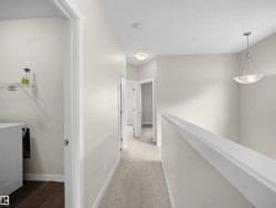 Upper-level hallway featuring neutral wall paint, carpet flooring, and a contemporary chandelier - 