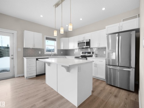 Modern kitchen featuring an island with a light countertop, white cabinetry, stainless steel appliances, grey subway tile backsplash, and wood-finish flooring - 8921 217 Street Nw, Edmonton, AB - Indoor Photo Showing Kitchen With Upgraded Kitchen