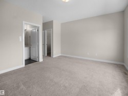 Spacious carpeted room featuring neutral wall tones, white trim, and a ceiling-mounted light fixture - 