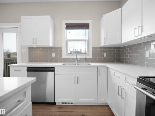 Modern kitchen featuring white shaker cabinetry, light-toned countertops, a gray subway tile backsplash, stainless steel appliances, and wood-finish flooring - 8921 217 Street Nw, Edmonton, AB - Indoor Photo Showing Kitchen With Upgraded Kitchen