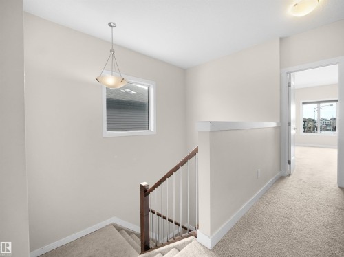 Upper-level landing featuring neutral carpeting, a staircase with dark wood handrail and white spindles, and a pendant light fixture - 8921 217 Street Nw, Edmonton, AB - Indoor Photo Showing Other Room