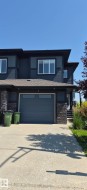 Contemporary townhouse exterior featuring dark siding, stone veneer accents, an attached garage, a paved driveway, and mature landscaping - 
