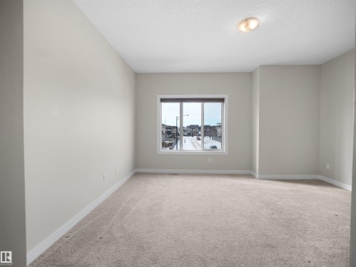 Spacious room with plush carpet flooring, neutral-toned walls, and a large window featuring a brown blind - 8921 217 Street Nw, Edmonton, AB - Indoor Photo Showing Other Room