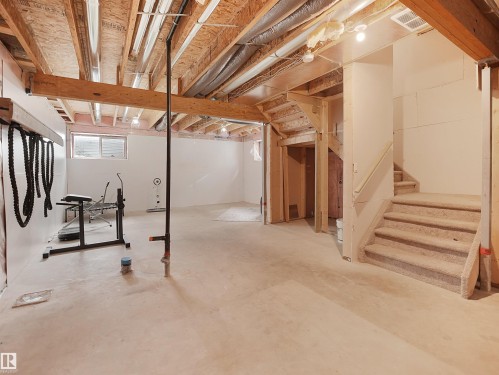 Unfinished basement featuring exposed wood joists, concrete flooring, egress window, and carpeted stairs with wood railing - 8921 217 Street Nw, Edmonton, AB - Indoor Photo Showing Basement