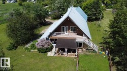 A-frame property featuring a brown exterior, a light-colored metal roof, and a prominent upper-level deck with white railings - 