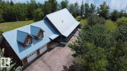 Expansive property featuring a brown-sided residence with a light blue metal roof, two dormers, and a three-car garage - 