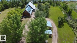 Property featuring a brown-sided structure with a light blue roof, multiple dormers, and surrounding mature trees - 
