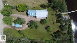 Expansive property featuring a main residence with light blue roofing, a detached accessory building, a private dock extending into the water, mature trees, and substantial green space - 