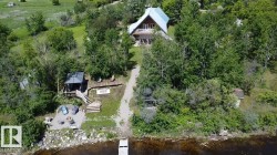 Waterfront property featuring a private dock, stone-paved patio with fire pit, expansive wooden deck with a gazebo, and a elevated residence with a balcony - 