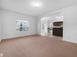 Expansive living area featuring neutral-toned carpeting and a large window with horizontal blinds - 