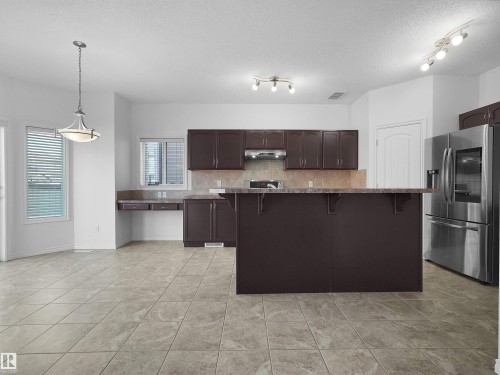 Open-concept kitchen and dining area featuring dark wood-finish cabinetry, stainless steel appliances, and a central island with an extended countertop - 2017 32A Street, Edmonton, AB - Indoor Photo Showing Kitchen With Upgraded Kitchen