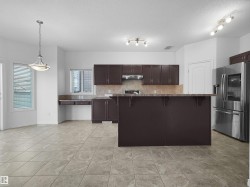 Open-concept kitchen and dining area featuring dark wood-finish cabinetry, stainless steel appliances, and a central island with an extended countertop - 