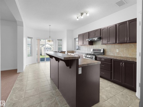 Kitchen featuring a central island with a breakfast bar, dark wood-finish cabinetry, a stainless steel range with overhead ventilation, and a tile backsplash - 2017 32A Street, Edmonton, AB - Indoor Photo Showing Kitchen With Upgraded Kitchen