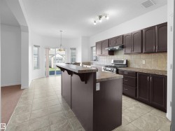 Kitchen featuring a central island with a breakfast bar, dark wood-finish cabinetry, a stainless steel range with overhead ventilation, and a tile backsplash - 