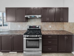 Kitchen featuring dark wood-finish cabinetry, stainless steel range with overhead hood, light-toned backsplash tiling, and speckled countertops - 