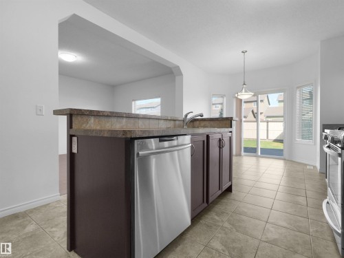 Kitchen featuring an integrated breakfast bar with a tile backsplash, stainless steel appliances, and tile flooring - 2017 32A Street, Edmonton, AB - Indoor Photo Showing Kitchen