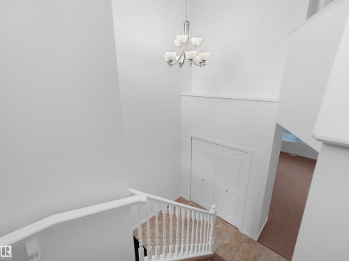 Foyer featuring a contemporary chandelier, white railings, tile flooring, and a bifold closet door - 2017 32A Street, Edmonton, AB - Indoor Photo Showing Other Room