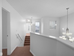 Bright upper landing featuring white walls and trim, brown carpeted flooring, and multiple windows with blinds - 