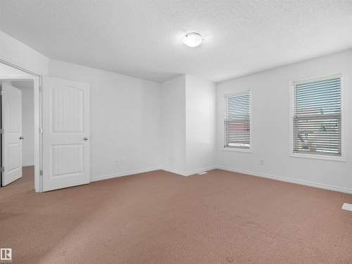 Spacious room featuring neutral carpet flooring, white painted walls, two windows with horizontal blinds, and a paneled interior door - 2017 32A Street, Edmonton, AB - Indoor Photo Showing Other Room
