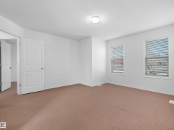 Spacious room featuring neutral carpet flooring, white painted walls, two windows with horizontal blinds, and a paneled interior door - 