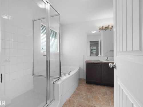 Bathroom featuring a glass-enclosed shower over a curved soaking tub, white wall tiling, a dark wood-finish vanity with a light countertop, a wall-mounted mirror, and decorative light fixture - 2017 32A Street, Edmonton, AB - Indoor Photo Showing Bathroom