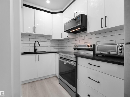 Contemporary kitchen featuring white cabinetry with dark hardware, black countertops, a subway tile backsplash, and light wood-finish flooring - 2017 32A Street, Edmonton, AB - Indoor Photo Showing Kitchen With Upgraded Kitchen