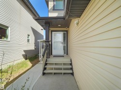 Front entrance featuring a covered porch with a stone-clad pillar, white storm door, and a three-step concrete staircase - 