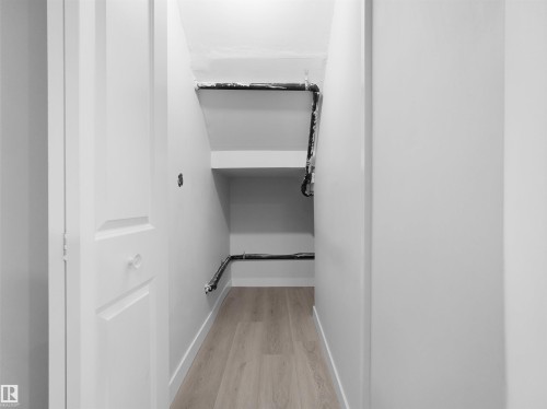 Under-stair storage area featuring integrated shelving, light wood-finish flooring, and crisp white walls - 2017 32A Street, Edmonton, AB - Indoor