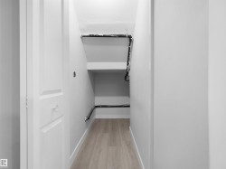 Under-stair storage area featuring integrated shelving, light wood-finish flooring, and crisp white walls - 