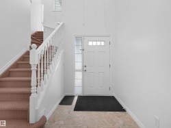 Entryway with a multi-pane front door, frosted sidelight, tile flooring, and a carpeted staircase with white balusters - 