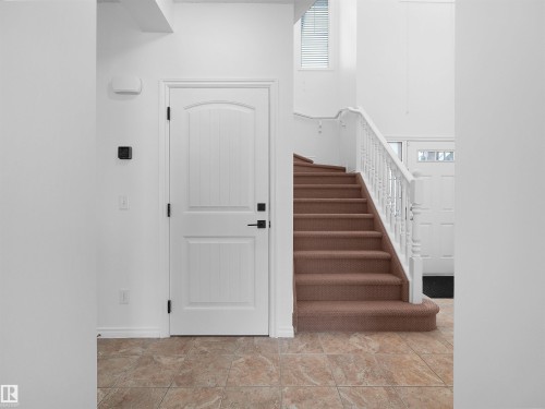 Foyer featuring tile flooring, a carpeted staircase with white balusters, and a white paneled door with matte black hardware - 2017 32A Street, Edmonton, AB - Indoor Photo Showing Other Room
