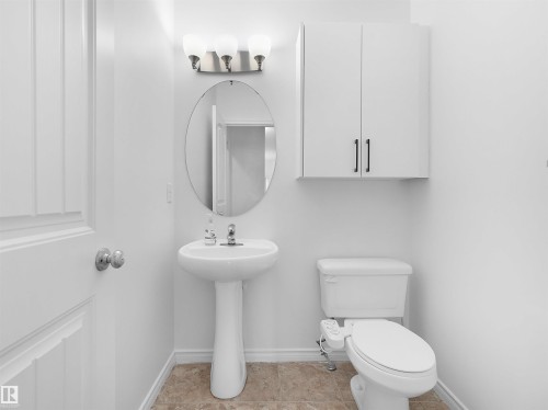 Pedestal sink with an oval mirror, modern vanity lighting, white wall-mounted cabinetry, and light-toned floor tiling - 2017 32A Street, Edmonton, AB - Indoor Photo Showing Bathroom