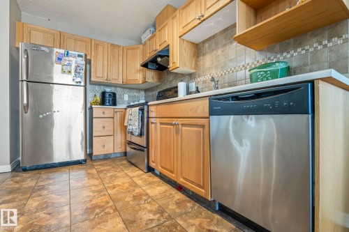 Kitchen featuring wood cabinetry, stainless steel appliances, tiled flooring, and a tiled backsplash - 412 5005 165 Avenue Nw, Edmonton, AB - Indoor Photo Showing Kitchen