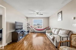 Spacious living area featuring wood-finish flooring, light neutral wall tones, and a ceiling fan - 