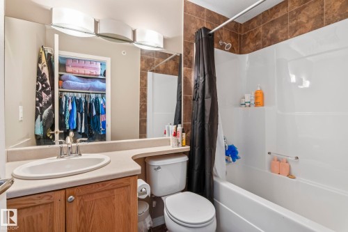 Bathroom featuring a combination tub and shower with tile surround, a single vanity with an integrated sink, wood-finish cabinetry, and overhead bar lighting - 412 5005 165 Avenue Nw, Edmonton, AB - Indoor Photo Showing Bathroom