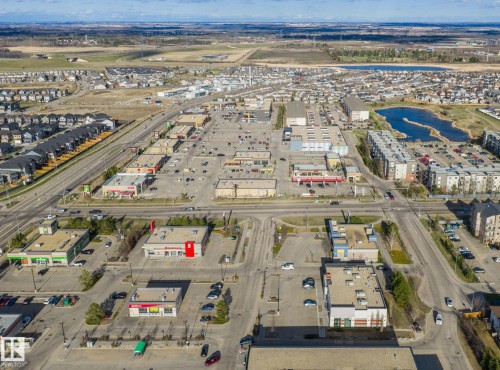 Aerial perspective showcasing a mixed-use development with commercial buildings, residential structures, and a natural water feature - 412 5005 165 Avenue Nw, Edmonton, AB - Outdoor With View