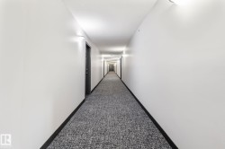 Hallway featuring wall-mounted sconce lighting, white walls, dark baseboards, and patterned carpet flooring - 