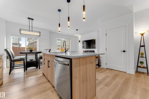 Open-concept kitchen featuring light wood-finish flooring, a central island with integrated stainless steel dishwasher, modern pendant lighting, and a dining area with a sliding glass door - 9 Hunter Place, Spruce Grove, AB - Indoor Photo Showing Kitchen With Upgraded Kitchen