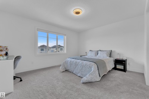 Spacious bedroom featuring light gray carpeting, crisp white walls, a large window with white framing, and a contemporary flush-mount ceiling light - 9 Hunter Place, Spruce Grove, AB - Indoor Photo Showing Bedroom