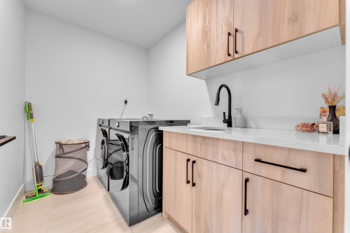 Laundry area featuring built-in cabinetry, a utility sink with a matte black faucet, and light wood-finish flooring - 9 Hunter Place, Spruce Grove, AB - Indoor Photo Showing Laundry Room