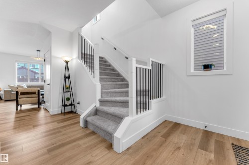 Open-concept entry foyer featuring wood-finish flooring, a carpeted staircase with black iron spindles, white baseboards, and a window with blinds - 9 Hunter Place, Spruce Grove, AB - Indoor Photo Showing Other Room