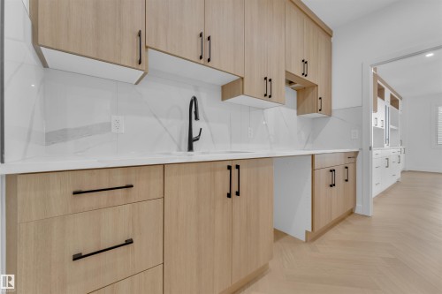 Kitchenette featuring light wood-finish cabinetry with matte black hardware, white countertops, and a white tile backsplash - 12 Dalquist Bay, Leduc, AB - Indoor Photo Showing Kitchen