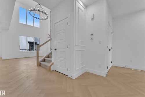 Two-story entry featuring wood-finish flooring in a herringbone pattern, a contemporary chandelier, and a wood and carpeted staircase - 12 Dalquist Bay, Leduc, AB - Indoor Photo Showing Other Room