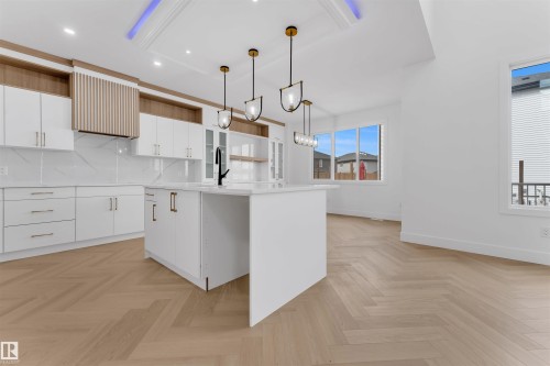 Contemporary kitchen featuring a large central island with seating, white cabinetry, integrated range hood with wood slat detailing, herringbone wood-finish flooring, and multiple windows - 12 Dalquist Bay, Leduc, AB - Indoor Photo Showing Kitchen
