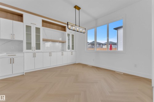 Herringbone wood-finish flooring complements a built-in cabinetry wall featuring white shaker-style doors, glass display cabinets, and light wood-tone open shelving - 12 Dalquist Bay, Leduc, AB - Indoor Photo Showing Other Room