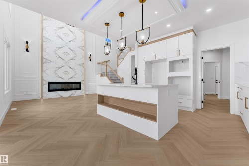 Open-concept living space featuring a chevron pattern wood-finish floor, a tall decorative fireplace surround, and a kitchen island with integrated shelving - 12 Dalquist Bay, Leduc, AB - Indoor Photo Showing Other Room