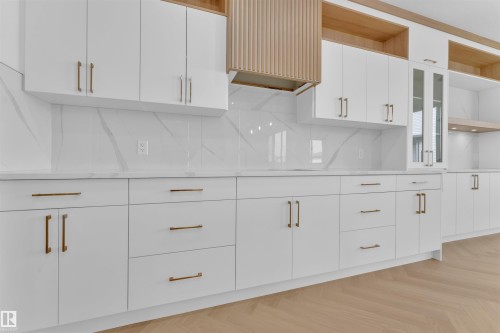 Modern kitchen featuring white cabinetry, bronze hardware, a white marble-look backsplash, and light wood-finish flooring - 12 Dalquist Bay, Leduc, AB - Indoor